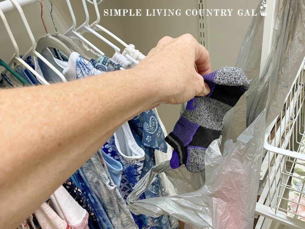 a hand putting socks into a plastic shopping bag in a closet