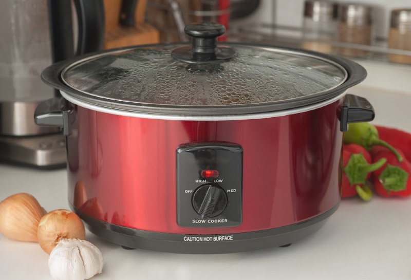 a red crock pot next to veggies on a counter