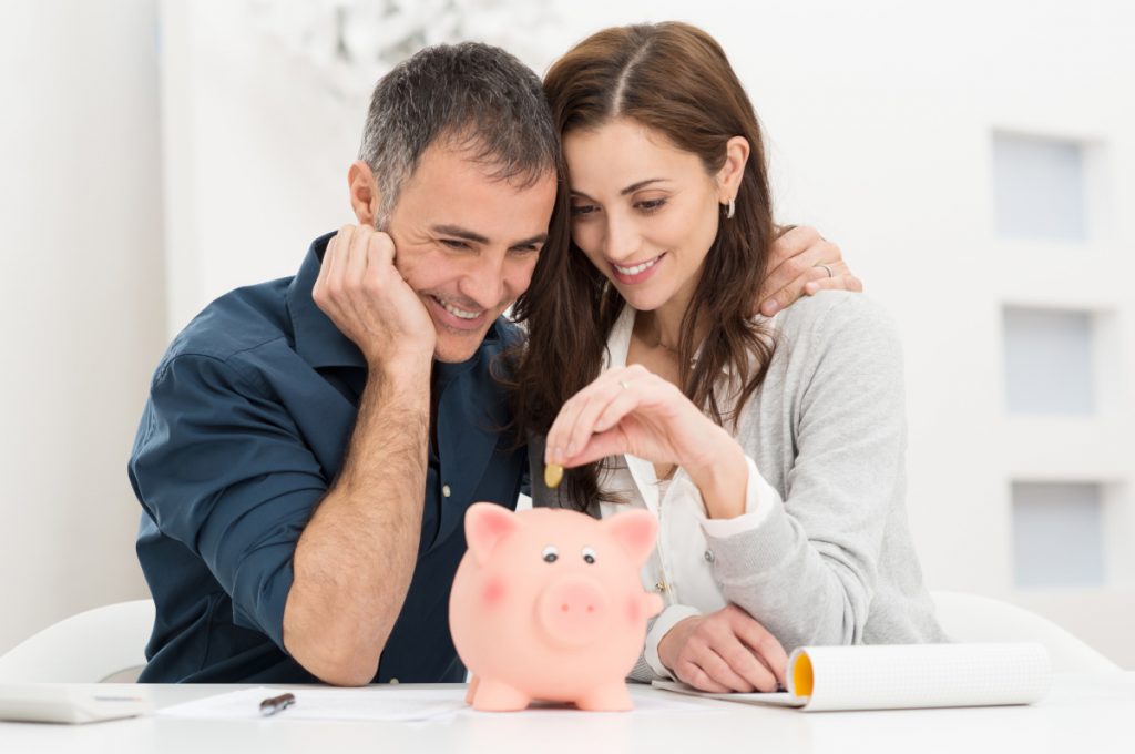 A couple puts a coin in a piggybank. They have learned how to save money this week.