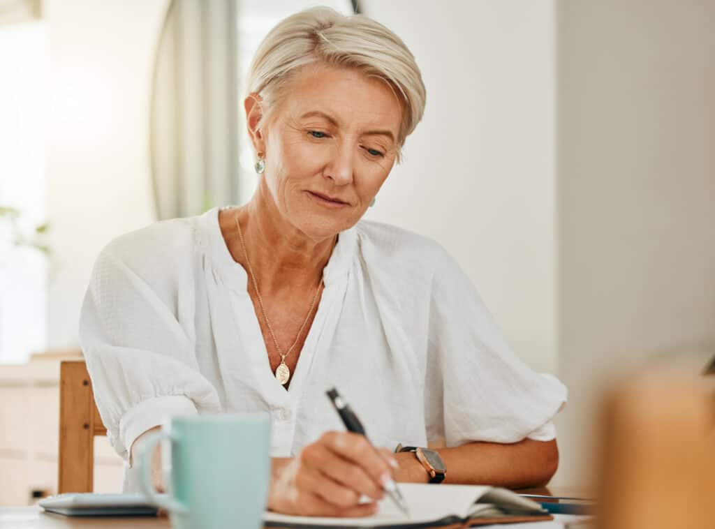 a senior woman reading over a to do list next to a blue cup of coffee