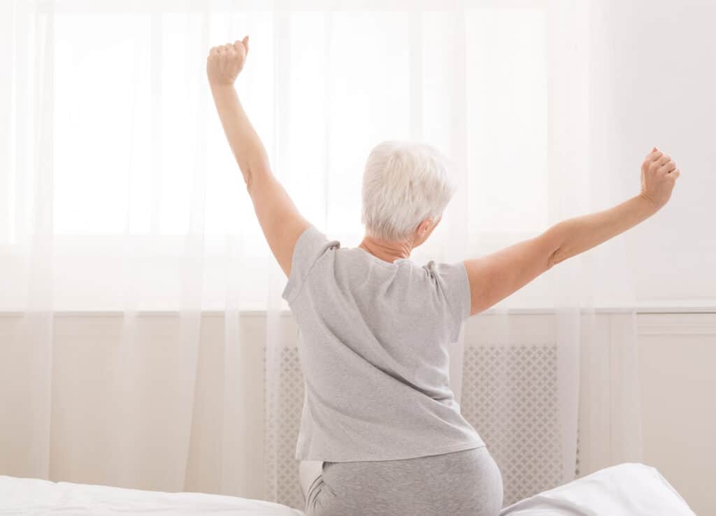 senior woman stretching in a bed from behind