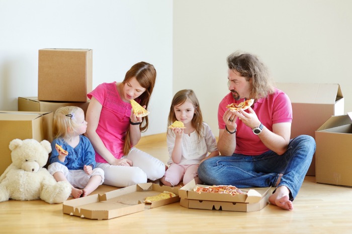 A family eats pizza surrounded by boxes after helping each other declutter. 