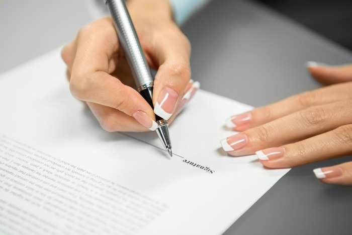 A woman signs a paper because dealing with paperwork immediately helps declutter kitchen countertops