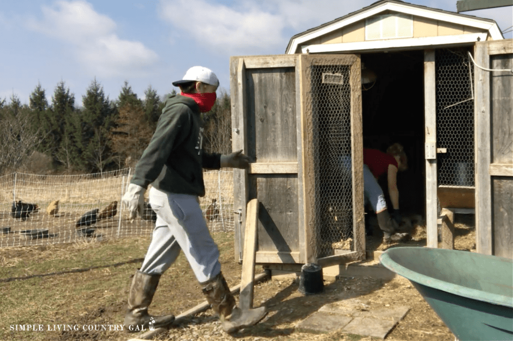 man in a red face bandana walking into a chicken coop with a woman inside cleaning