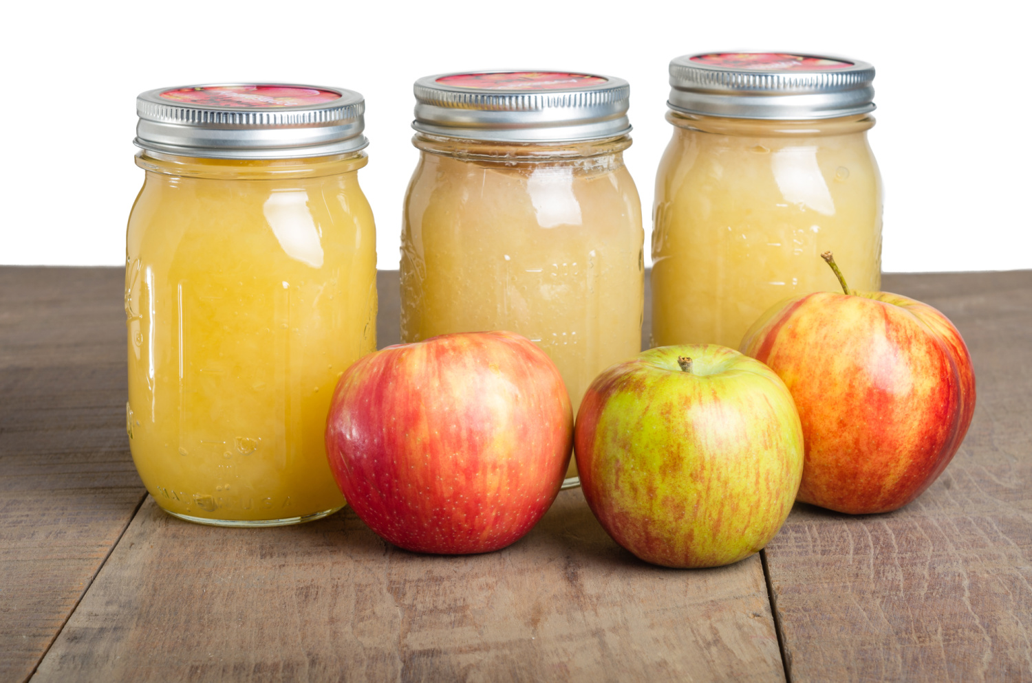 3 jars of canned applesauce sitting in front of three apples