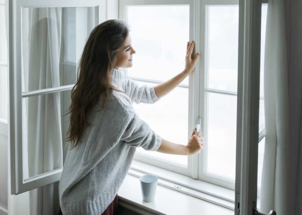 Woman is opening window to look at beautiful snowy landscape outside