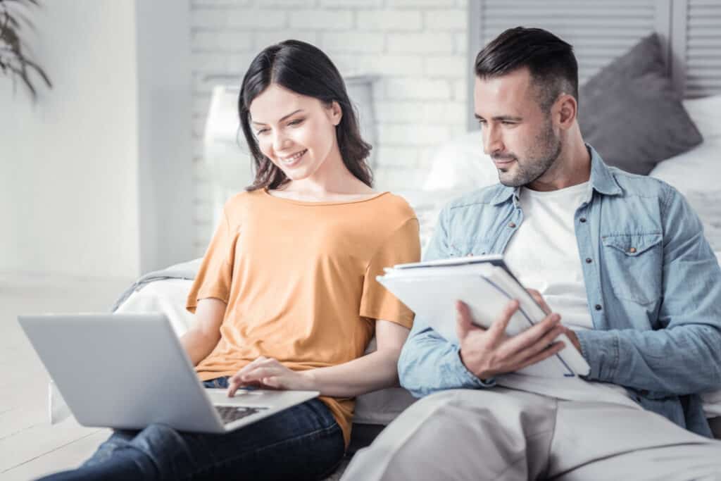 couple sitting on a couch planning projects on paper and laptop