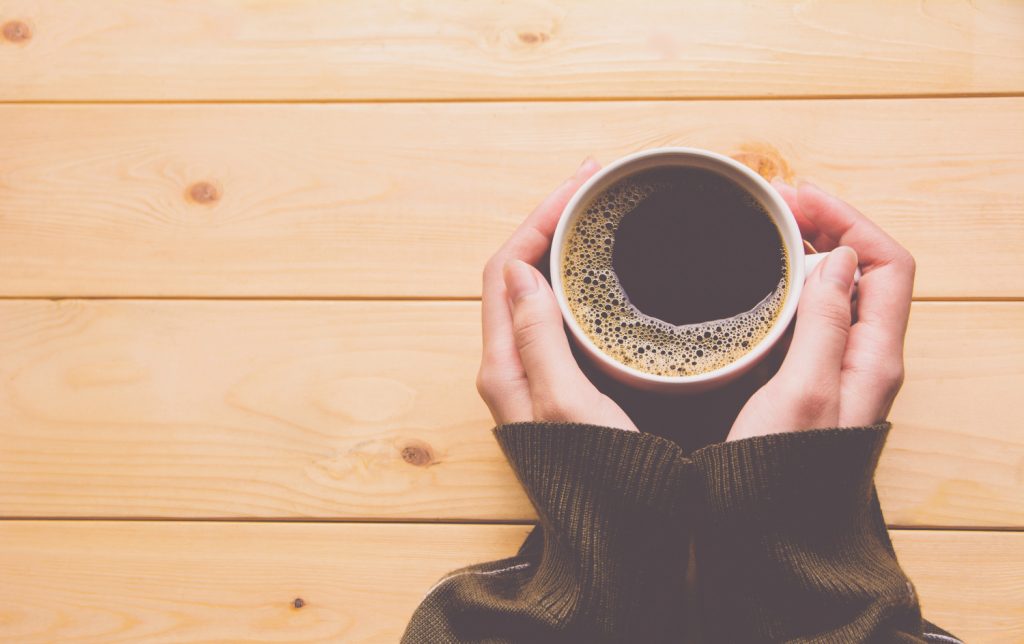 hands on a table holding a cup of coffee