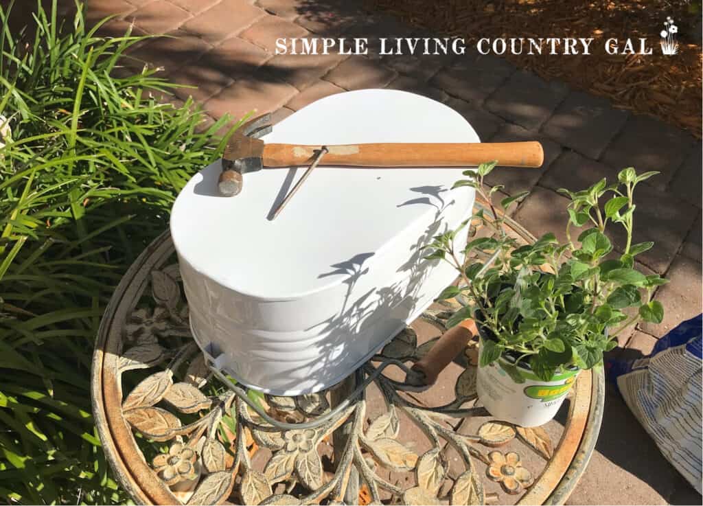 a metal container with a nail and hammer on the top and a small potted plant next to it