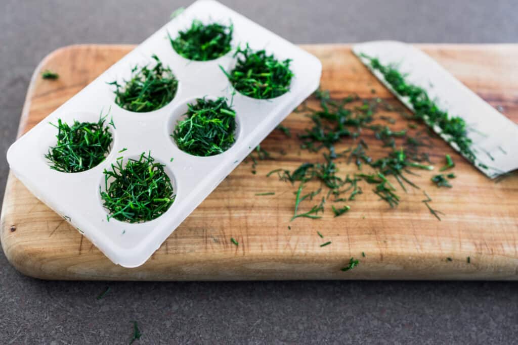 an ice cube tray filled with fresh chopped herbs to freeze