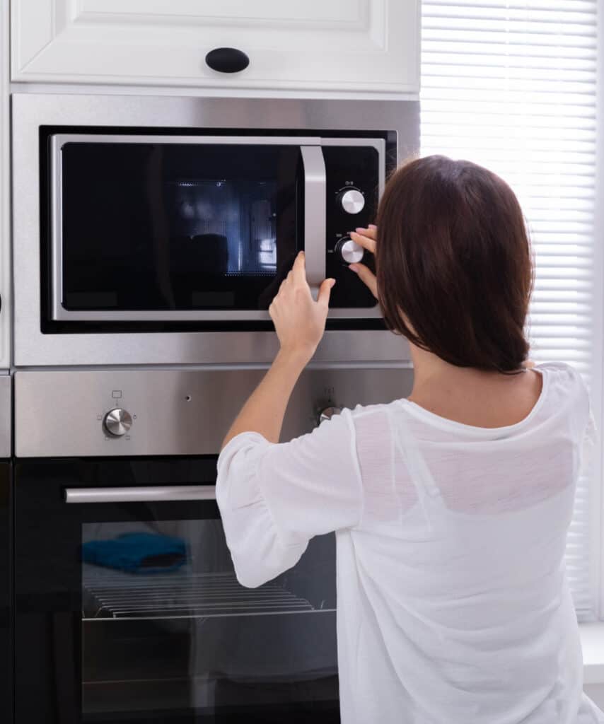 a woman in a white shirt pushing the buttons on a microwave oven