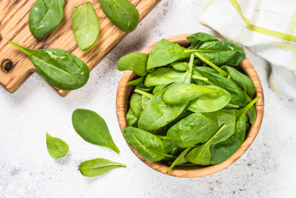 Home grown spinach leaves in wooden bowl on white background. Top view.