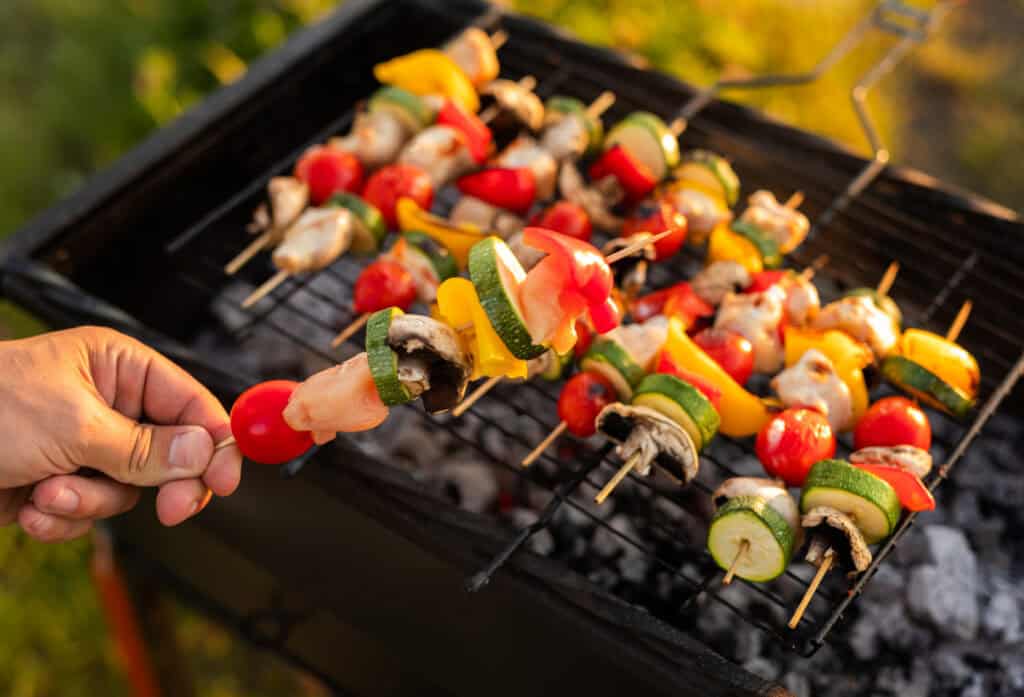 vegetables cooking on a grill with a hand holding a scure