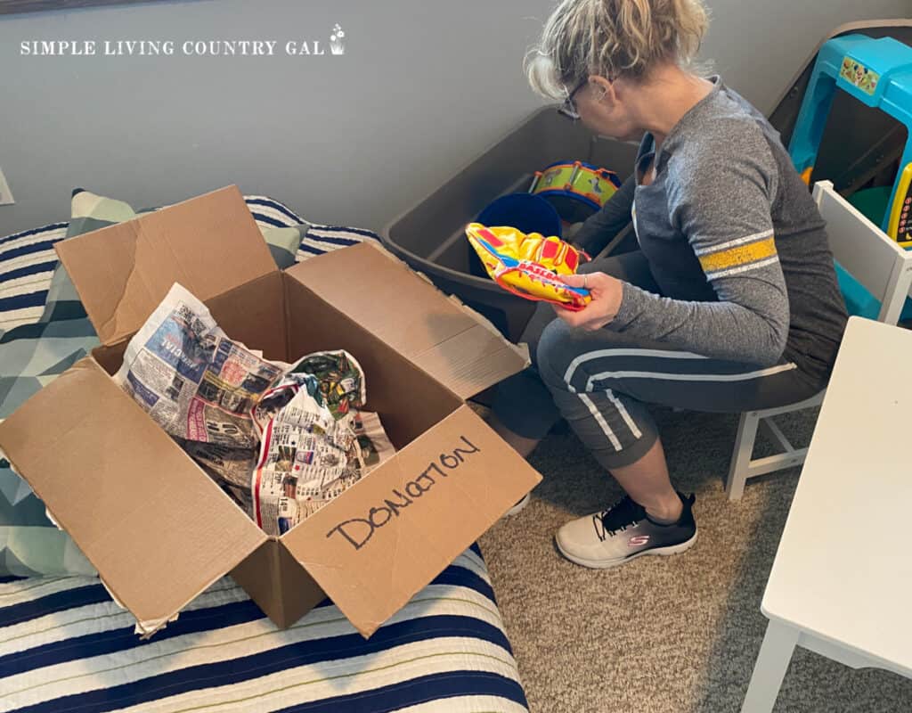 a woman putting toys into a donation box in a kids bedroom