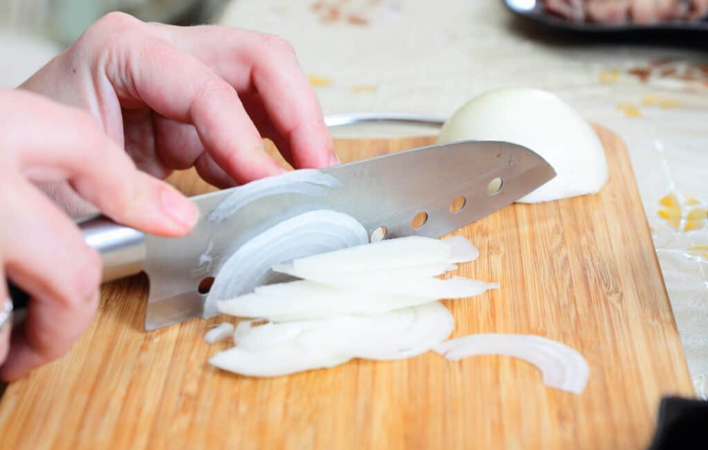 hands chopping a fresh white onion on a cutting board