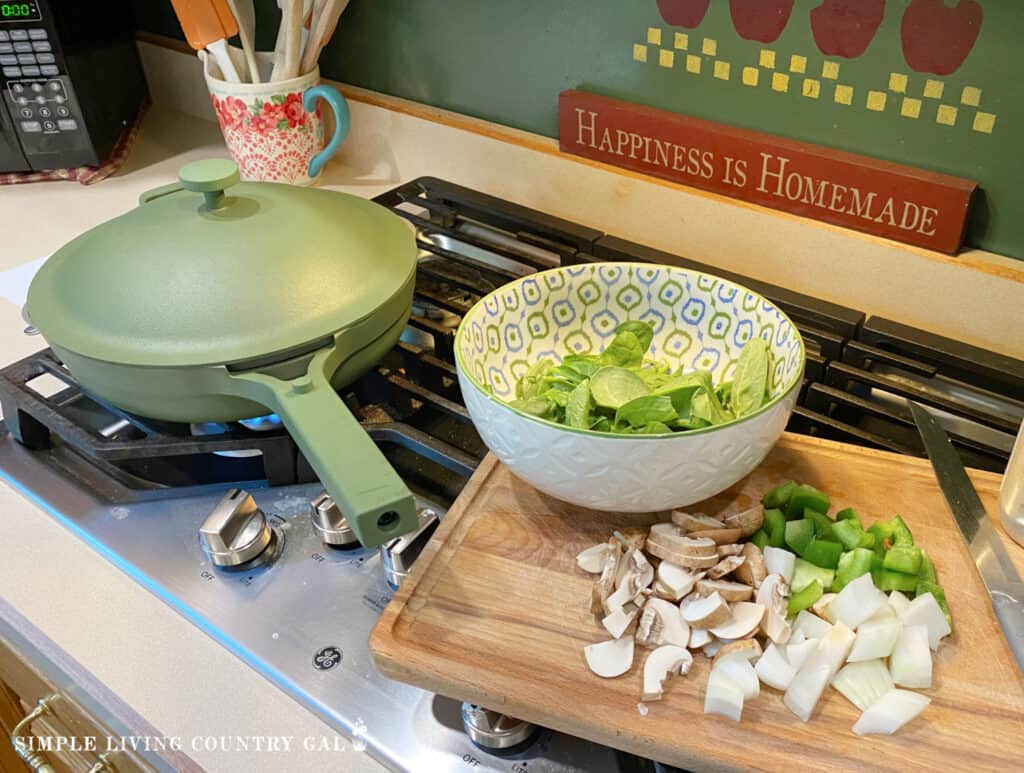 spinach in a bowl next to chopped veggies neat to a pan 