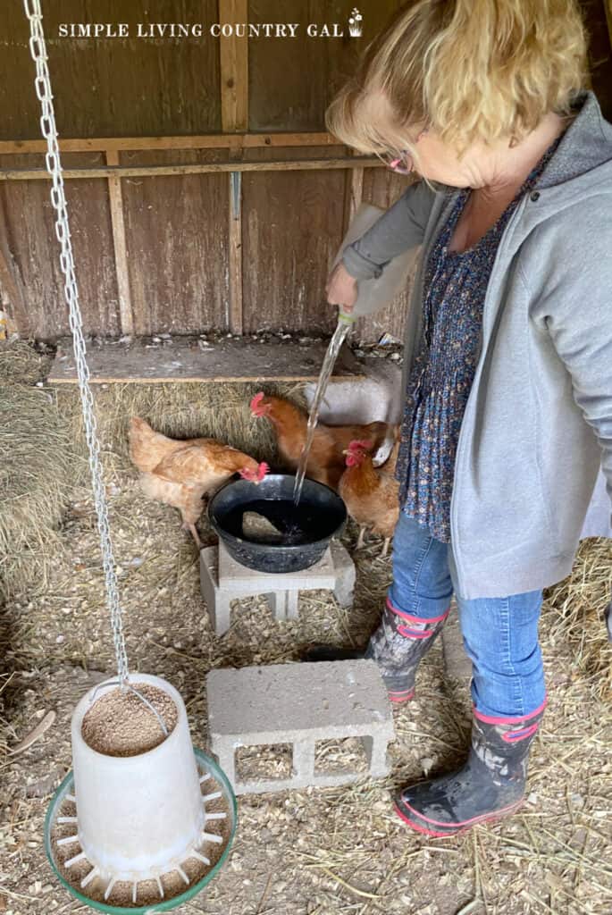 a woman pouring fresh water into a bowl inside of a chicken coop