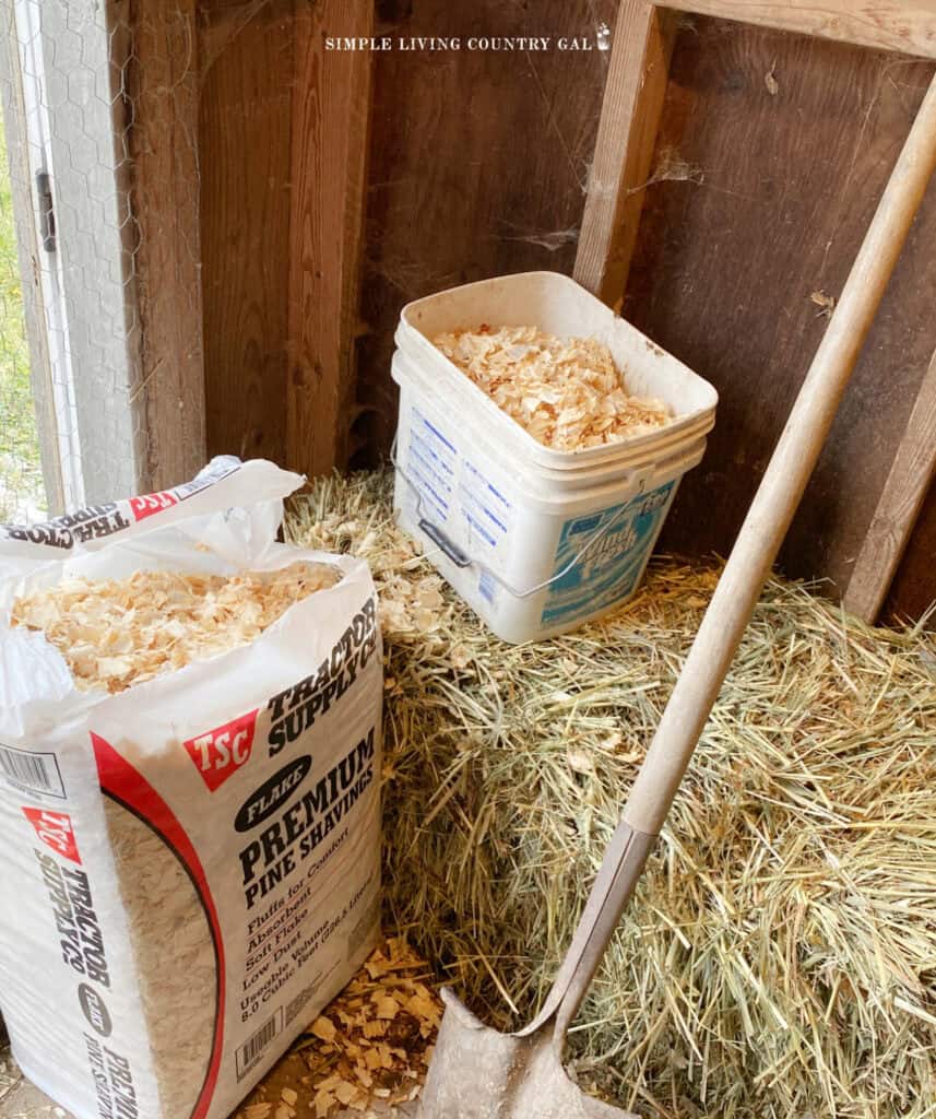 a bag of wood shavings next to a bucket and a shovel inside of a chicken coop