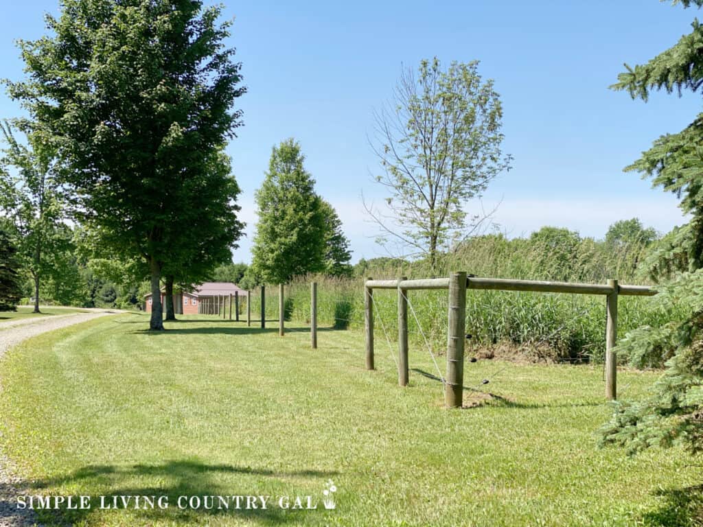 a fence near a pasture with trees and a small barn in the background