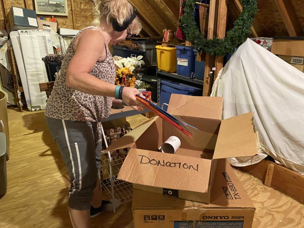 a woman sorting clutter into donation boxes in an attic