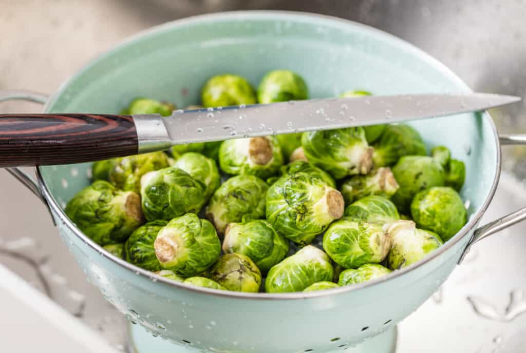 a colander of fresh Brussels sprouts with a knife over the top