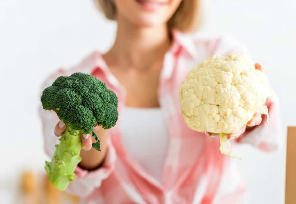 woman holding a head of broccoli and cauliflower