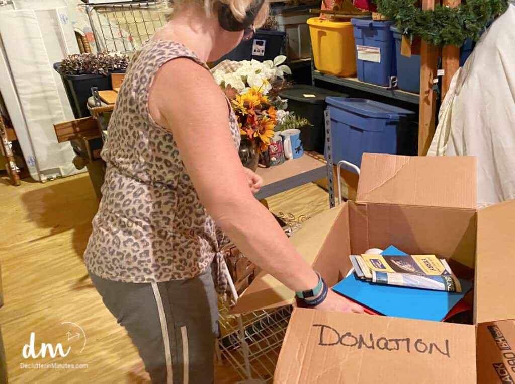 woman putting items into a box labeled donation in a cluttered attic. 