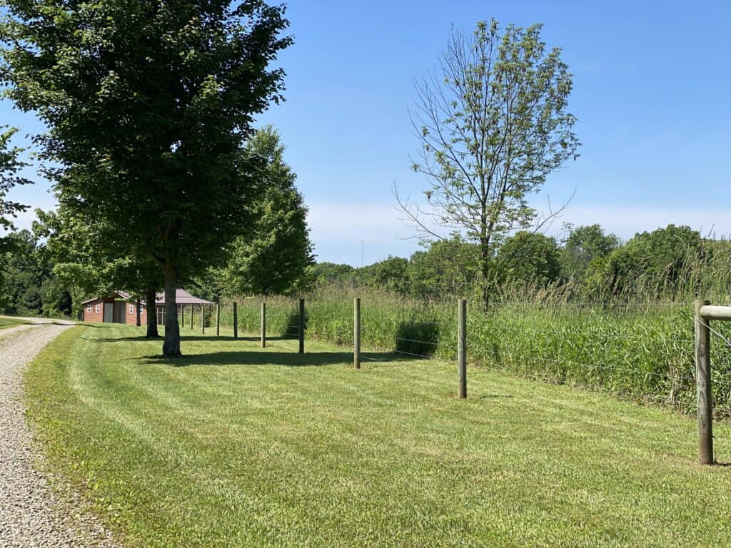 a pasture fence and a barn along a gravel driveway