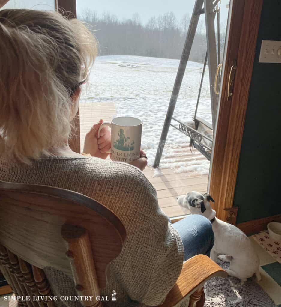 a woman holding a cup of coffee looking out at the snow