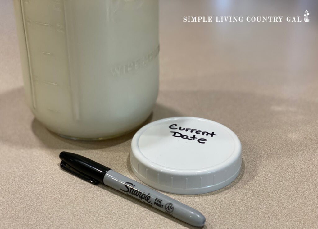 a mason jar of goat milk with a black marker by a lid with _current date_ on it
