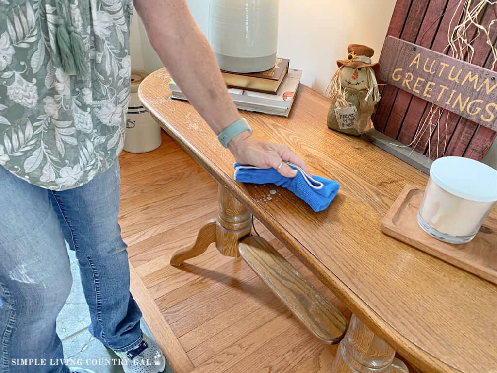 a woman cleaning a wood table in a home with cleaner