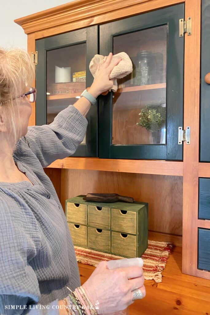 a woman cleaning the glass on a green and wood cabinet