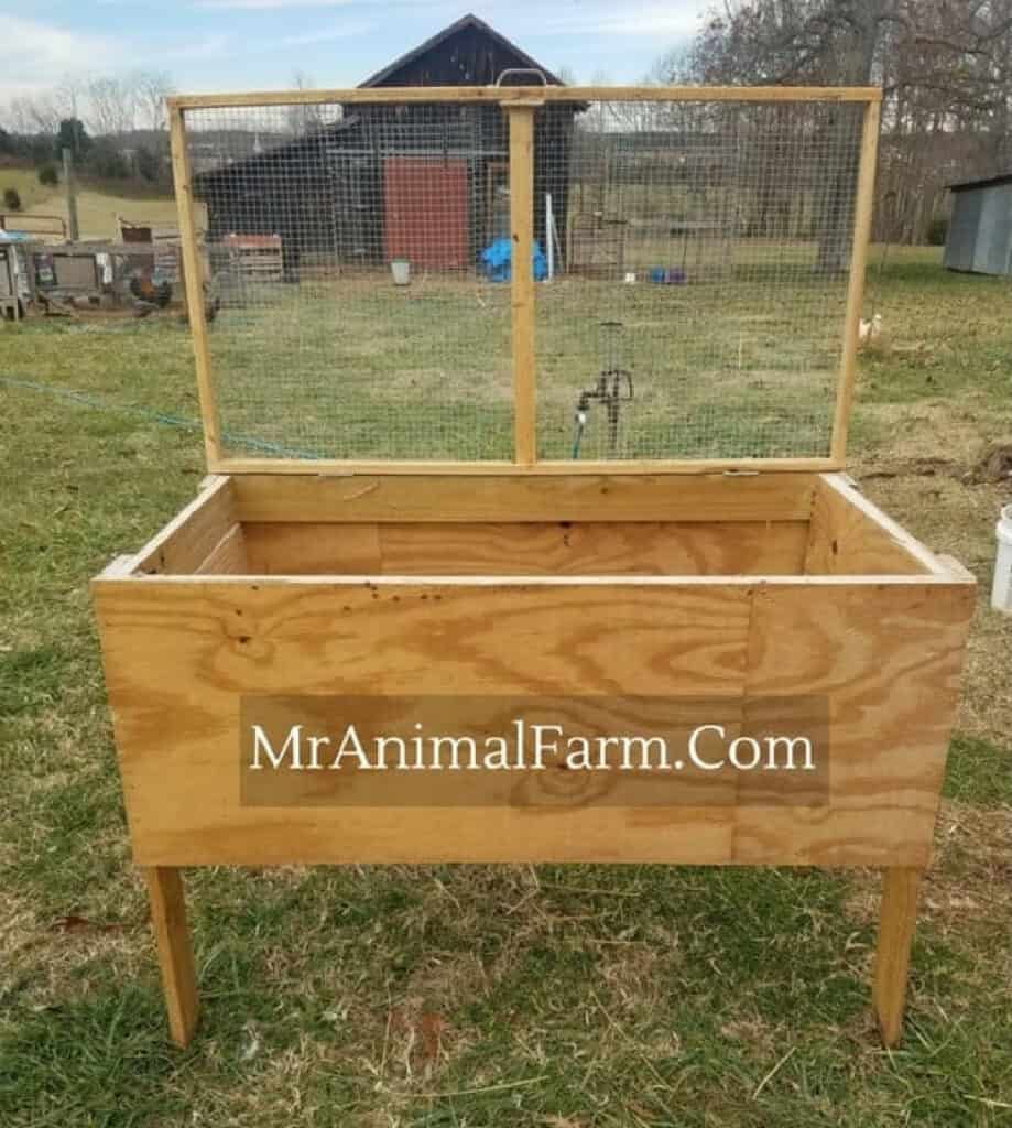 a wooden box on 4 legs with the lid up that has chicken wire on it. Has the words "MrAnimalFarm.com" on the box