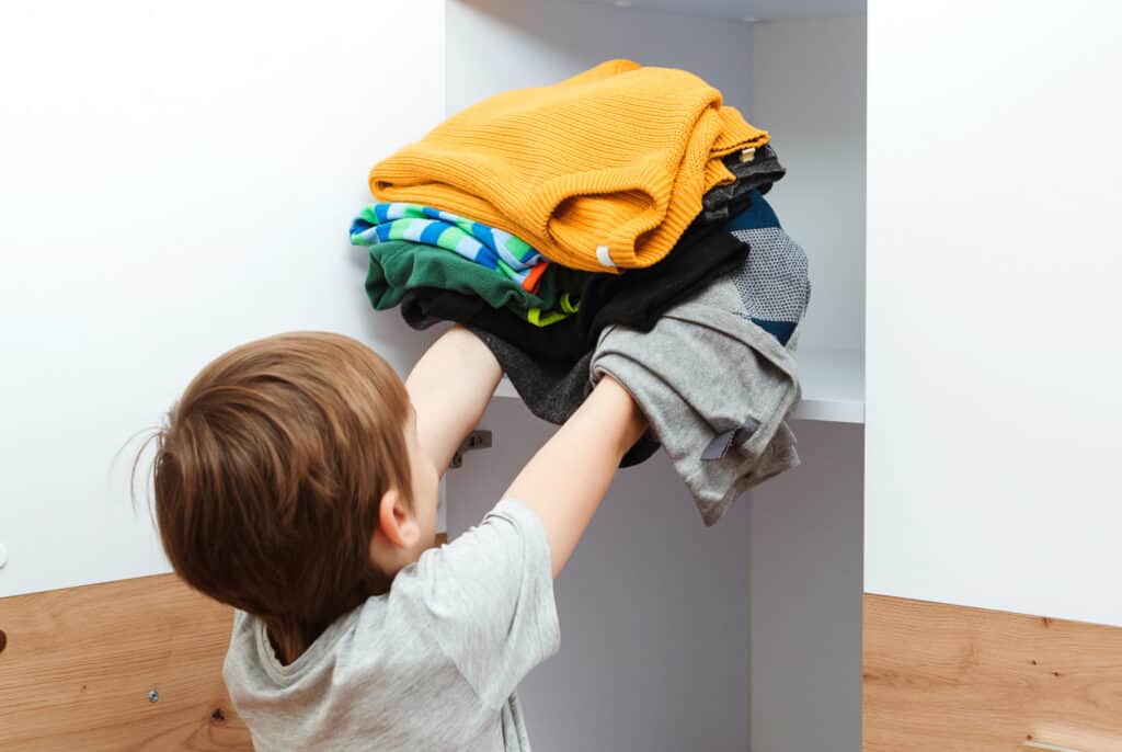 a young boy putting clothes into a cabinet