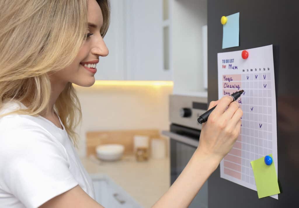 Young woman checking to do list on refrigerator door in kitchen