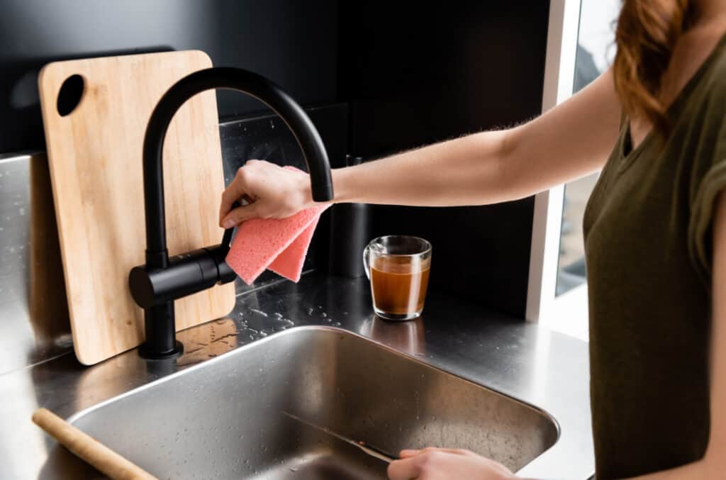 woman wiping down a steel sink with a pink sponge
