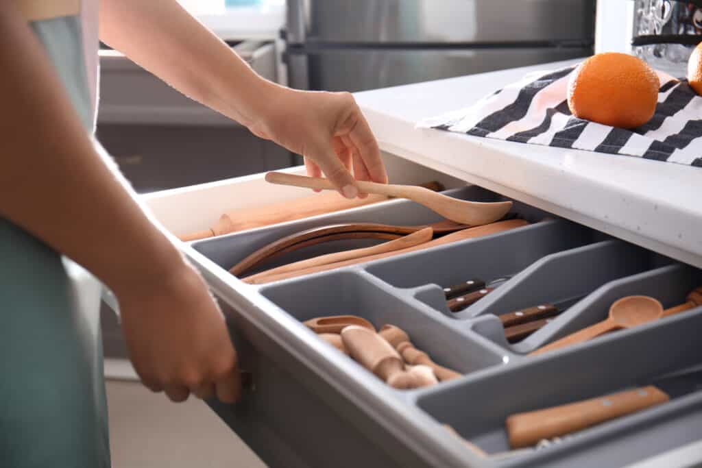 Woman putting wooden spoon into kitchen drawer