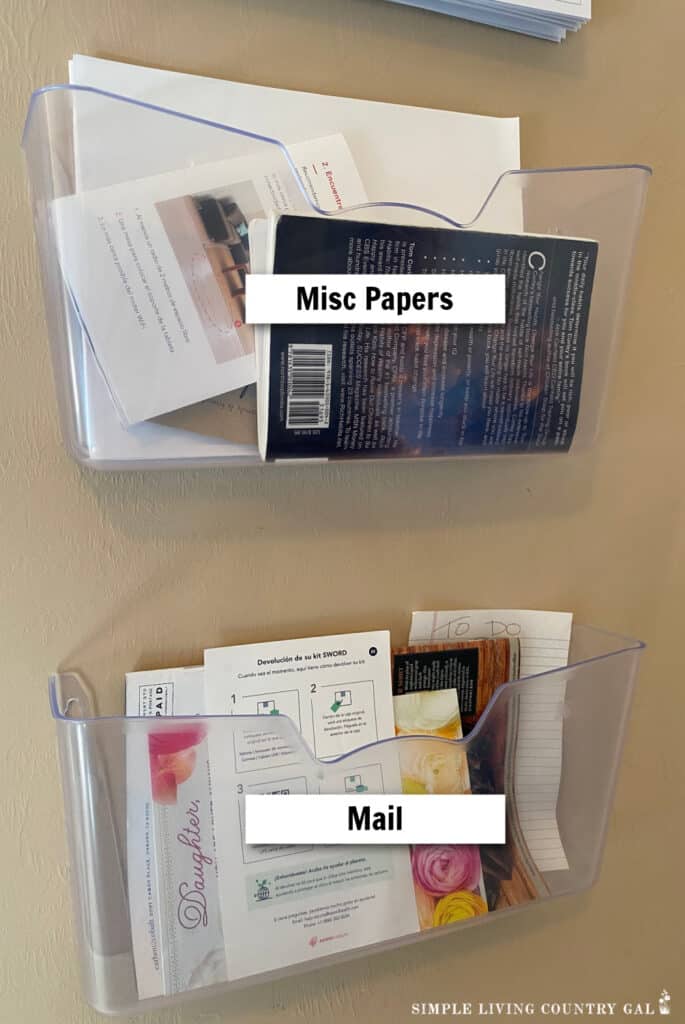 two clear organizers on a wall in a simplified kitchen. One holding misc papers and one holding mail 
