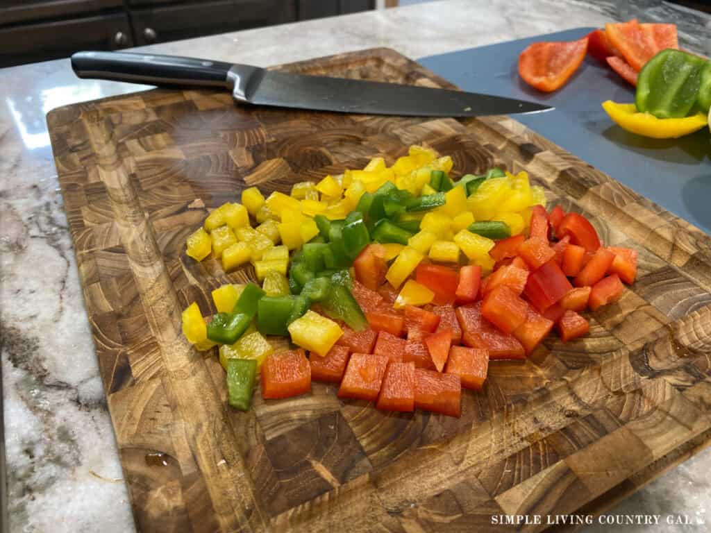 diced pepper of yellow, green, and red on a cutting board next to a knife