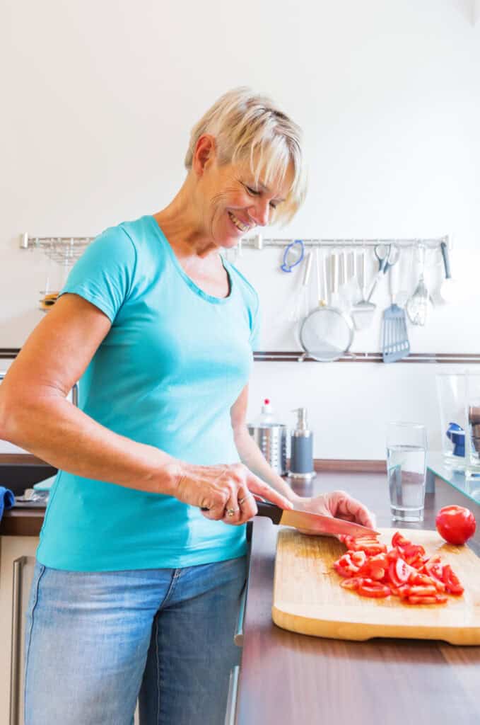 midlife woman standing at a counter in the kitchen dicing tomatoes for a meal 