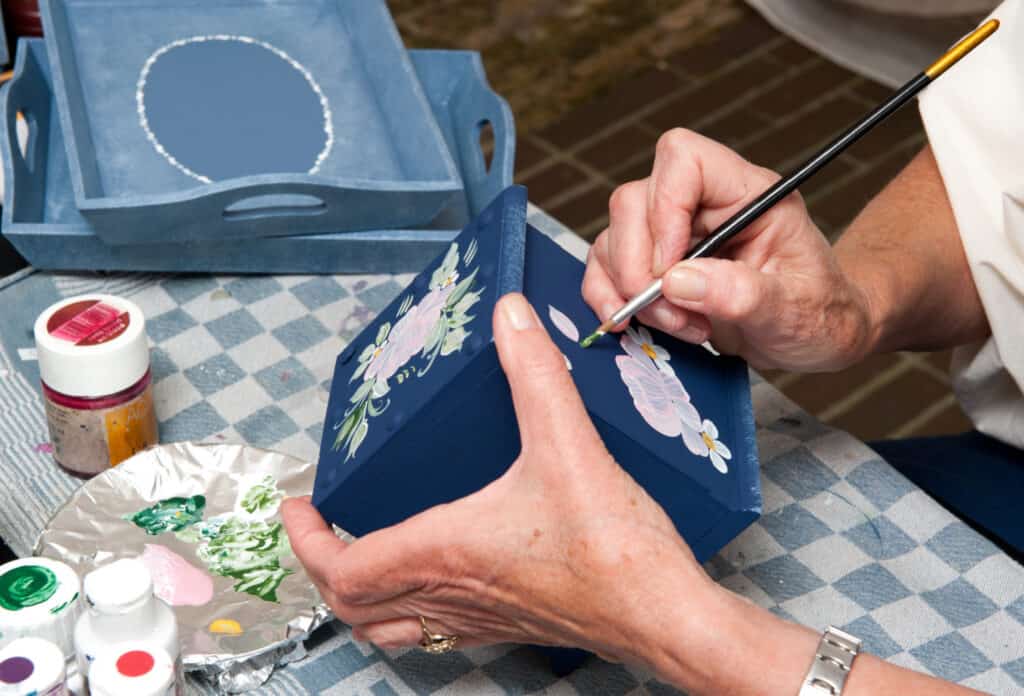 A woman painting a flower onto the front of a blue box