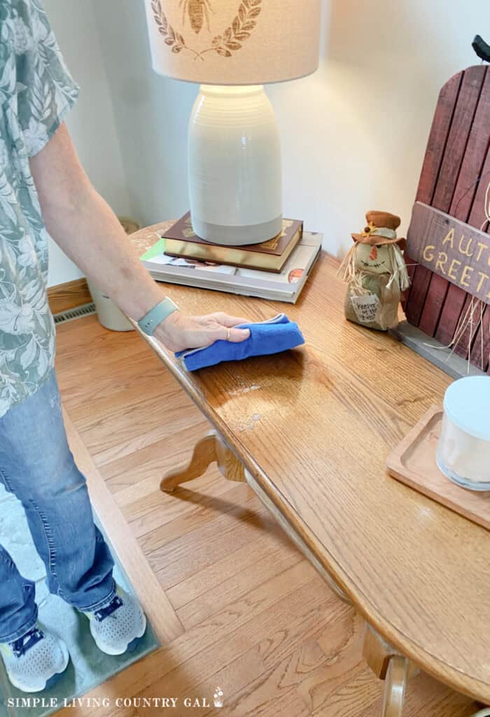 a woman using a blue cloth to dust a wood table 