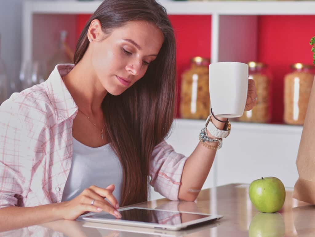 a woman holding her coffee making notes on an ipad for her weekly menu