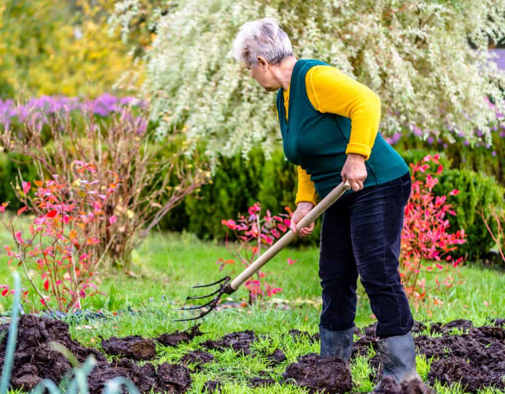 an older woman putting compost onto a garden