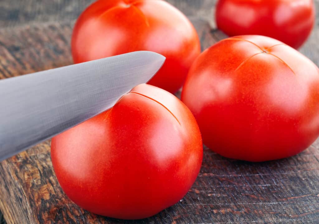 a knife cutting a fresh tomato on a brown cutting board