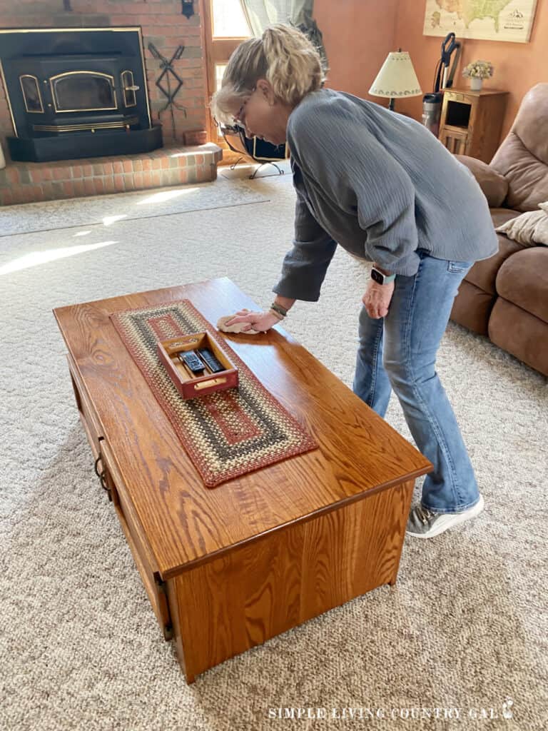a woman dusting a coffee table with a rag 