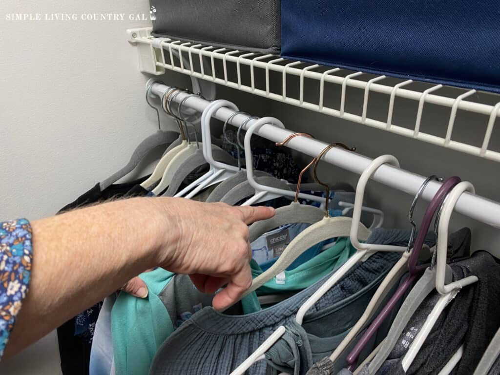 a hand pointing to a hanger on a rod in a closet that is facing backward