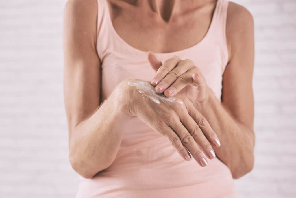 a woman in pick rubbing herb infused lotion into her hands
