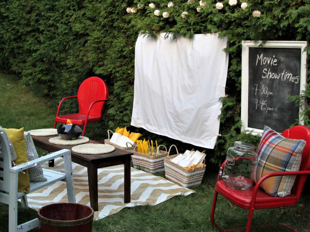 a sheet hanging outside with chairs, movie player, and chalkboard with Movie Showtimes written on it