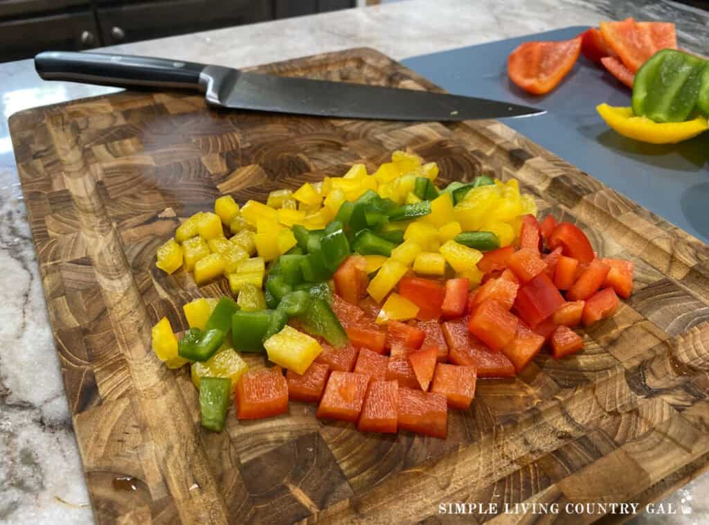 a wood cutting board with yellow, green, red diced peppers and knife on top
